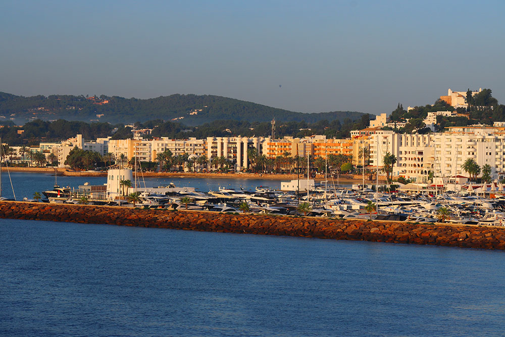 Scenic view of Santa Eulalia, Ibiza, featuring a vibrant marina, luxury yachts, and a coastal skyline at sunset